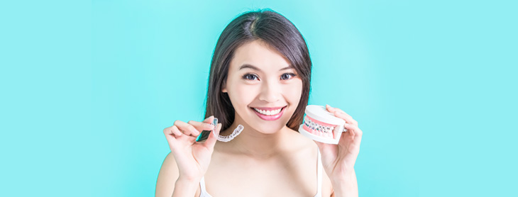 Young woman smiling and holding a plastic model of jaw with braces