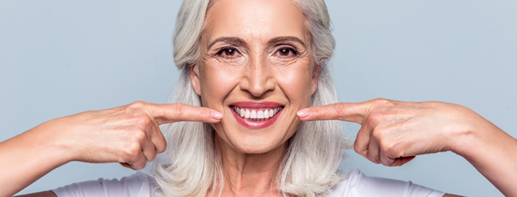 Middle aged woman smiling and pointing to her teeth
